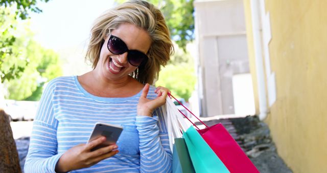 Laughing woman holding shopping bags and smartphone outdoors - Download Free Stock Images Pikwizard.com