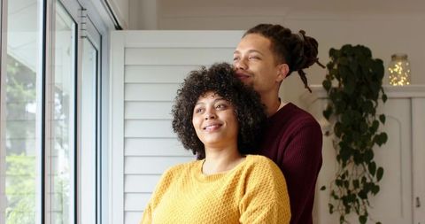Couple Embracing Beside Sunlit Window with Knit Sweaters and Indoor Plant