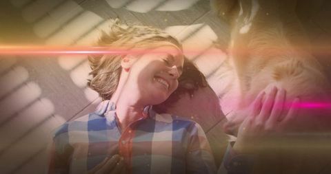 Smiling woman lying on floor petting dog in sunlit home with warm pink lens flare