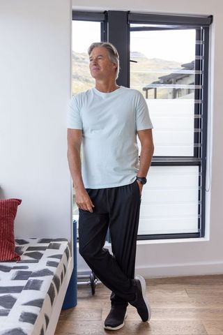Mature man standing and gazing through black-framed window in modern living room