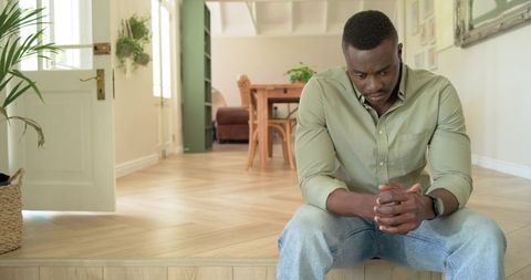 African american man sitting on entryway step looking contemplative in bright modern home