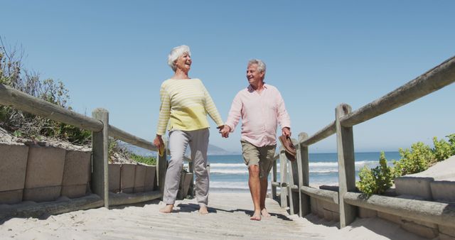 Happy senior caucasian couple holding shoes in their hands walking on path leading to the beach - Download Free Stock Photos Pikwizard.com