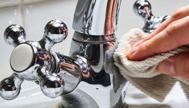 Close-up wiping and polishing chrome bathroom faucet with beige cloth and water droplets