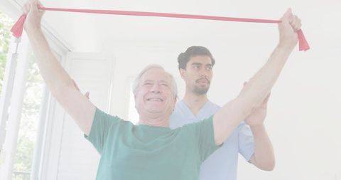 Senior man performing resistance band shoulder exercise with therapist assistance