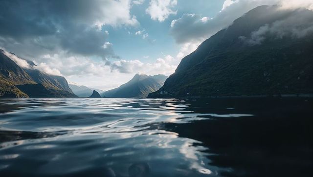 Reflecting water leading toward distant sunlit peaks in dramatic fjord landscape