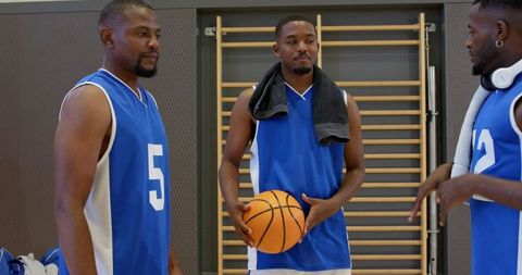 Basketball teammates holding ball and talking, wearing blue jerseys, towels and headphones