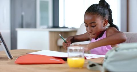 Focused african american girl studying at kitchen table with notebook and tablet