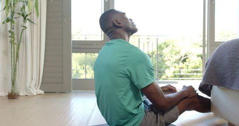 African American man stretching on bedroom mat by balcony during sunlit morning yoga routine
