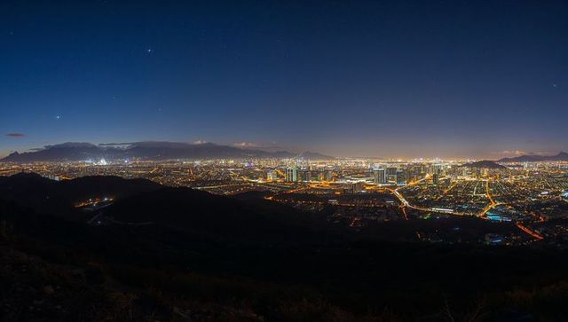 Panoramic city skyline glowing over hillside at night with illuminated grid and towers