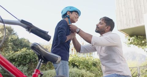 Father Helping Son Adjust Helmet Outdoors with Red Bicycle