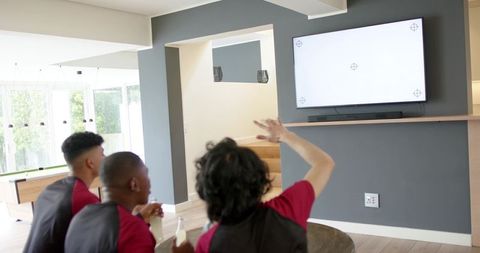 Diverse friends cheering while watching game on wall-mounted tv in modern rec room