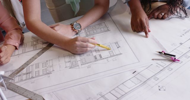 Group of architects collaborating over large residential building blueprints. Useful for content related to construction projects, architectural teamwork, design planning, and engineering. Ideal for illustrating themes of collaboration, precision, and project management in the architecture and construction industries.