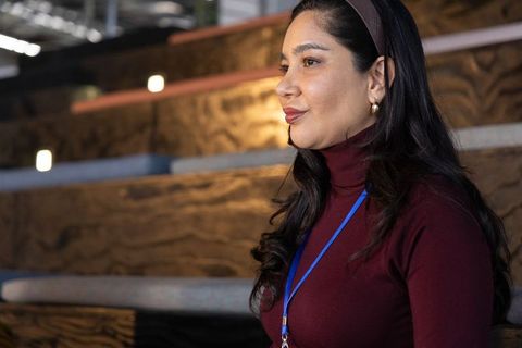 Contemplative conference attendee on wooden tiered benches wearing burgundy turtleneck