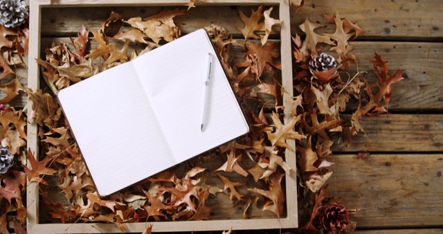 Notebook with pen with copy space lying on dry leaves and wooden floor. Autumn, halloween and writing unaltered.