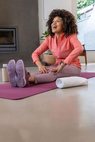 African american woman stretching on purple mat at home smiling after workout