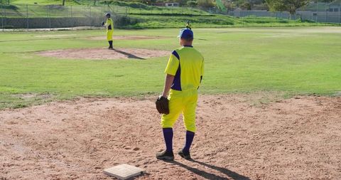 Baseball players standing near base on sunny diamond wearing yellow and blue uniforms