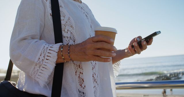 Mature Woman Holding Coffee Cup and Smartphone Near Ocean - Download Free Stock Images Pikwizard.com