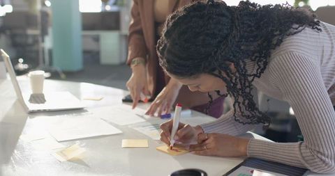 Diverse female coworkers collaborating with sticky notes during office brainstorming