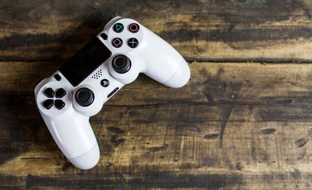White gaming controller resting on wooden table, useful for articles on gaming culture, console equipment advertisements, or blog posts about video game trends and technology.