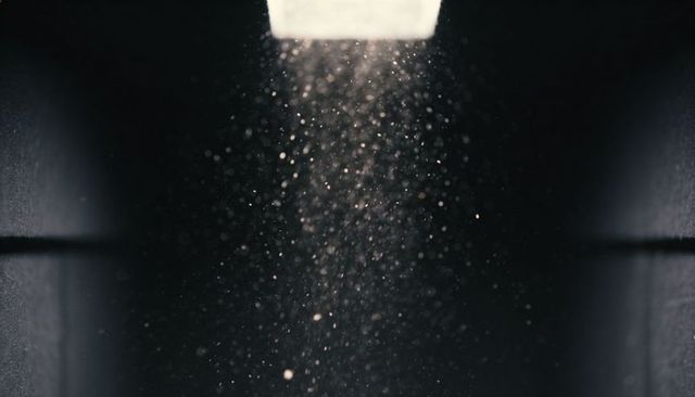 Illuminated dust column falling through narrow shaft with dramatic light beam and bokeh