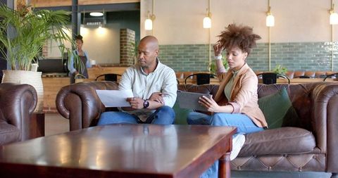 Diverse coworkers collaborating on documents and tablet in modern coworking lounge
