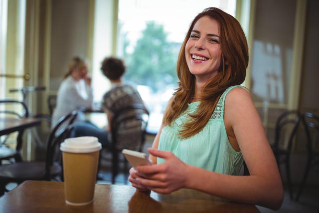 Young woman enjoying coffee while using her mobile phone in a cozy cafe. Ideal for lifestyle blogs, social media content, advertisements for coffee shops, and technology-related promotions.
