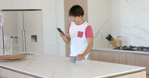 Asian college student checking phone in modern kitchen