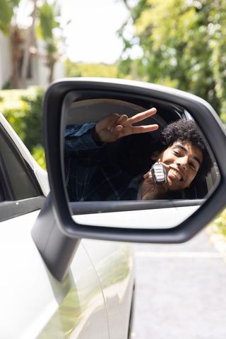 Young african american man showing car key and peace sign in side-view mirror