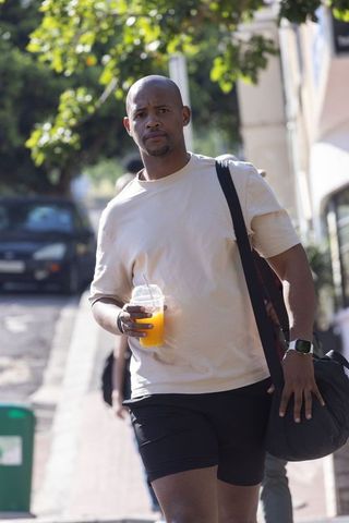 African american man walking uphill holding orange juice carrying shoulder bag