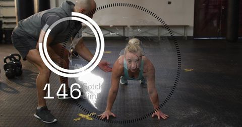 Female athlete holding plank while coach guiding in functional gym with kettlebells hud