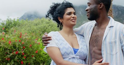 Diverse couple embracing in lush garden with misty mountain backdrop