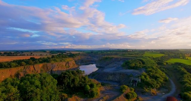 Picture showcasing aerial view of picturesque countryside featuring a quarry lake at sunset. The serene setting includes lush greenery, rocky cliffs, and expansive views under a colorful evening sky. Ideal for use in travel brochures, outdoor adventure blogs, nature documentaries and background visuals emphasizing tranquility and natural beauty.