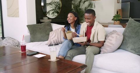 Friends Sharing Takeout with Chopsticks on Cozy Sofa