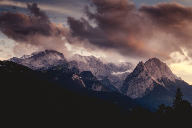 Spectacular view of a mountain range with dramatic dark clouds at sunset. Suitable for use in promotions for travel and adventure destinations, outdoor activity advertisements, or as a breathtaking wallpaper and background for desktop or mobile devices. Ideal for conveying serenity, grandeur, and the beauty of nature.