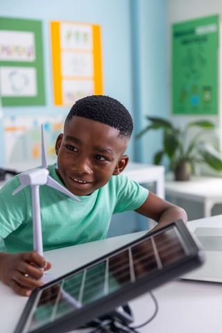 African american schoolboy exploring renewable energy with wind turbine and solar panel
