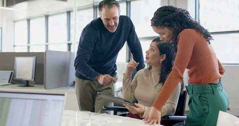 Multicultural team collaborating around tablet and charts in modern open-plan office