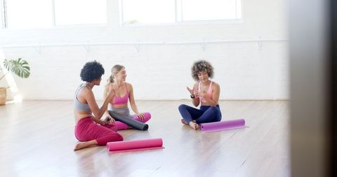 Diverse women relaxing in yoga studio with technology