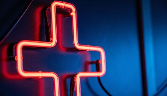 Glowing red neon cross sign with visible tubing and power cables in storefront
