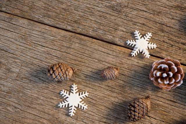 Pine cones and snowflakes arranged on a wooden plank create a rustic and festive holiday scene. Perfect for Christmas-themed designs, winter decorations, and seasonal promotions. Ideal for use in greeting cards, holiday invitations, and festive marketing materials.