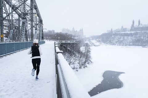 Solo jogger running across snow-covered bridge with frozen river and city skyline
