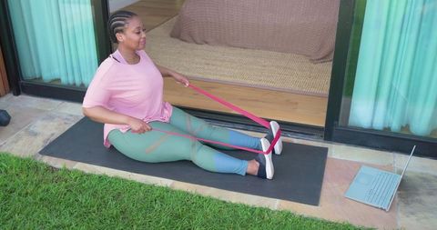 African american woman exercising with resistance band on patio following online class