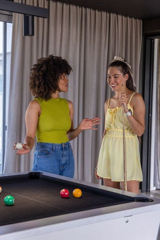Two friends chatting and playing billiards in modern lounge with black-felt pool table