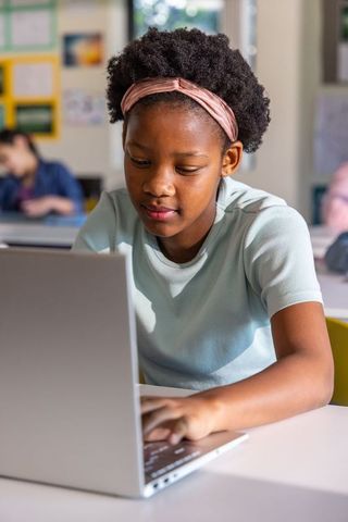 African American Teen Studying on Laptop at School Desk, Concentrating on Online Learning
