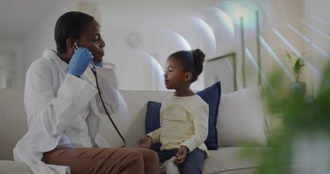 Black clinician listening to young girl's heartbeat during warm home pediatric checkup