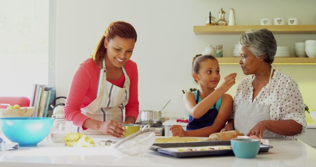 A grandmother, mother, and daughter are bonding while baking in a contemporary kitchen. The family exhibits happiness and togetherness as they prepare food. Suitable for illustrating family activities, cooking, parenting, and multi-generational relationships in advertising, blogs, or social media.