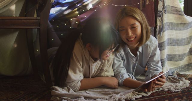 Asian mother and daughter smiling while using digital tablet under blanket fort at home - Download Free Stock Photos Pikwizard.com
