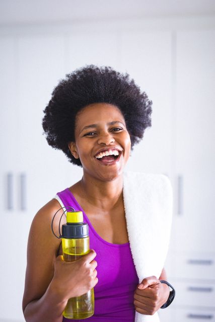 Portrait of happy african american mid adult woman with water bottle and napkin at home. unaltered, lifestyle, fitness, healthy lifestyle, wellbeing.