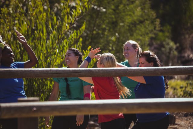 Group of fit women giving high five to each other at an outdoor boot camp on a sunny day. Ideal for promoting teamwork, fitness programs, outdoor activities, and healthy lifestyles. Perfect for use in advertisements, fitness blogs, and motivational content.
