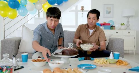 Father and Son Celebrating 18th Birthday at Home with Cake and Snacks