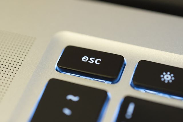 This image showcases a close-up view of the Esc key on a modern laptop keyboard, with the keys illuminated by soft backlighting. The image is useful for technology-themed materials, illustrating articles about computing, hardware design, or user interface design. It can also serve as a visual for educational content on keyboard functions and shortcuts.